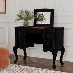 a small black desk with a mirror on it and a potted plant in the corner