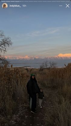 a person walking down a dirt road next to tall dry grass and mountains in the distance