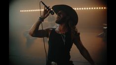 a man with long hair wearing a hat and holding a microphone