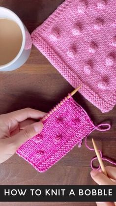 a person is knitting on a table with a cup of coffee and pink crochet