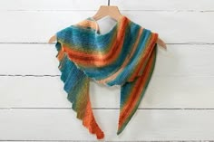 a multicolored shawl hanging on a wooden hanger against a white wall