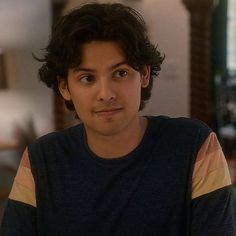 a young man with curly hair sitting in front of a table and looking at the camera