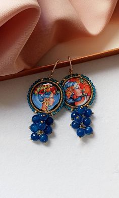 Sicilian style earrings made of: - Lava rock tiles decorated on a side with Sicilian Ceramic; - Faceted stones (6 mm), blue color; - Brass open hooks. Tile Diameter: 25 mm Lenght : 5,5 cm / 2,17 inches oSHIPPINGo Your order will be shipped within 1-3 business days from your purchase. You can choose between 2 shipping methods: STANDARD MAIL (NOT TRACEABLE) It is a cheap and fast shipping method, but NOT TRACEABLE. Chapeau Atelier is not responsible for any postal disruptions, delays or losses. RE Handmade Blue Cluster Earrings For Gift, Traditional Handmade Multicolor Chandelier Earrings, Artisan Blue Beaded Round Earrings, Handmade Byzantine Round Earrings, Traditional Sicilian Jewelry, Sicilian Ceramic Heads, Rock Tile, Bohemian Blue Enamel Earrings, Sicilian Style