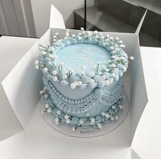 a blue cake in a white box with flowers on it's sides and the words happy birthday written on top