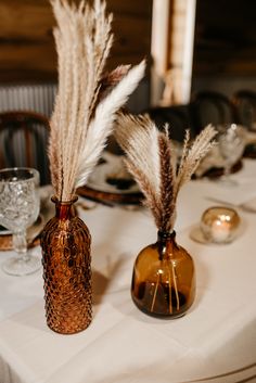 there are two vases with feathers in them on top of a white table cloth