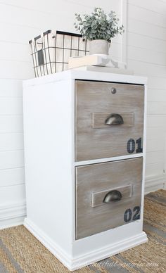 a white and gray filing cabinet with two drawers on top of it, next to a potted plant