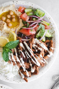 a white plate topped with meat, rice and veggies next to a fork