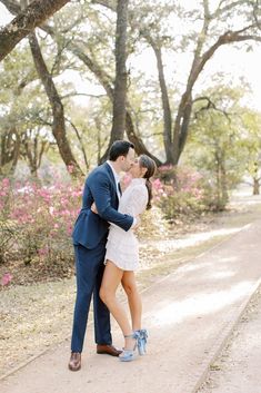 a man and woman are kissing in front of some trees with pink flowers on the ground