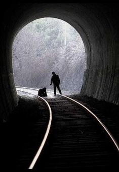 a man standing next to a dog on train tracks in a tunnel with snow falling off the ground