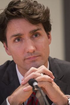 a man in a suit and tie sitting at a table with his hand on the microphone