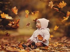 a baby sitting on the ground surrounded by leaves