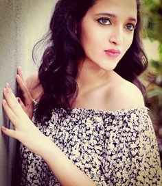 a woman with long black hair and blue eyes posing for a photo in front of a wall