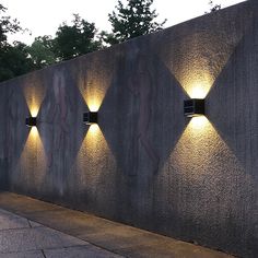 three lights are lit up on the side of a concrete wall with trees in the background