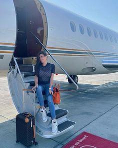 a woman sitting on the steps of an airplane with her luggage in front of it