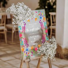 a welcome sign with baby's breath flowers on it sitting on top of a wooden easer