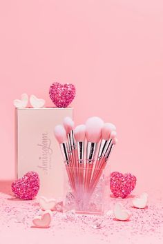 the pink makeup brushes are in a clear container with hearts on it and scattered confetti