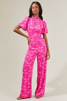 Glamorous get-togethers just wouldn't be the same without the Clever Floral Mock Neck Wide Leg Jumpsuit! A mock meets a gathered seam that's framed by flirty ruffle cap sleeves. It maintains a sleek fit, leading to wide leg pants. The back features covered rouleaux buttons at the neck and a keyhole cut out topping a zipper closure. Perfect to wear for any event this summer! - Mock neck- Puff sleeves- Wide legs- Keyhole- Color: Fuchsia multiSize + Fit - Model is 5'8" and wearing size XS- Measurem Feminine Fitted Floral Jumpsuits And Rompers, Pink Ruffled Jumpsuits And Rompers For Date Night, Spring Fitted Ruched Jumpsuits And Rompers, Fitted Ruched Jumpsuits And Rompers For Spring, Feminine Fitted Short Sleeve Jumpsuits And Rompers, Color Fuchsia, Cut Out Top, Wide Legs, Wide Leg Jumpsuit