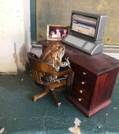 a frog sitting in a chair next to a desk with a computer on top of it