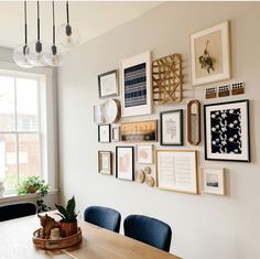 a wooden table topped with blue chairs next to a white wall covered in framed pictures