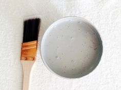 a white bowl with a wooden handle next to a brush