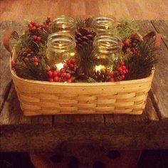 mason jars filled with pine cones and candles are sitting in a basket on a wooden table