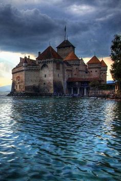 an old castle sitting on top of a body of water under a dark cloudy sky