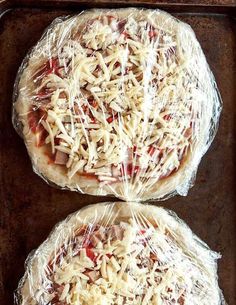 two uncooked pizzas wrapped in plastic wrap