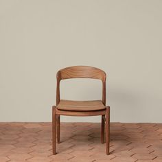 a wooden chair sitting on top of a brick floor next to a wall with a white wall in the background