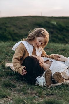 a mother and daughter laying on the ground playing with each other in an open field