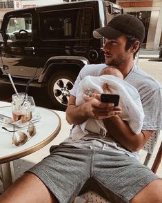 a man holding a baby while sitting at a table with a cell phone in his hand