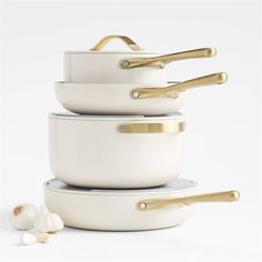 three white pots with gold handles stacked on top of each other next to some garlic