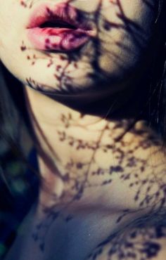 a woman's face and body covered in black ink with branches on her chest