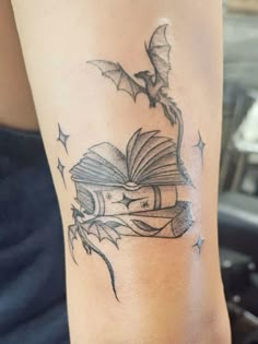 a tattoo on the arm of a woman with a book and flying bats above it