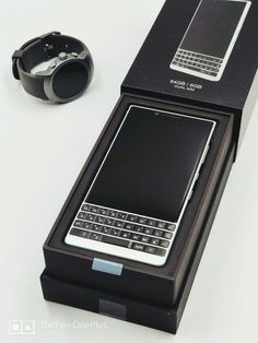 an open box with a cell phone in it and a watch on the table next to it