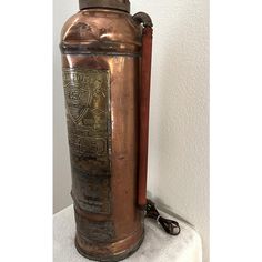 an old fashioned copper flask is sitting on top of a white tablecloth with a metal chain hanging from it's side