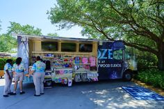 two people are standing in front of a food truck that sells pizzas and other items