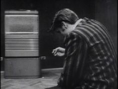 a young boy sitting on the floor in front of an old fashioned refrigerator and reaching for something