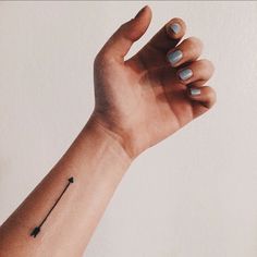 a woman's arm with a small black arrow tattoo on the left side of her wrist