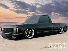 a black truck parked on top of a sandy beach next to the ocean at sunset