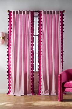 a pink chair sitting next to a window covered in pink curtain panels with scalloped edges