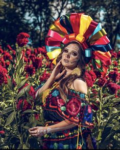 a woman wearing a colorful headdress standing in a field of flowers with her face painted like a skeleton