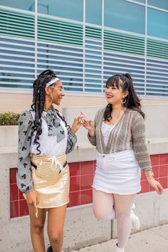 two women dressed in costumes standing next to each other on the sidewalk, one holding her hand out