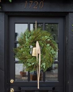 a wreath on the front door of a house with a bell hanging from it's side