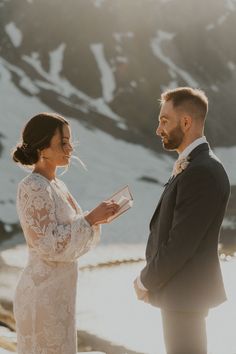 a bride and groom standing next to each other in front of snow covered mountains during their wedding ceremony