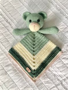 a crocheted teddy bear sitting on top of a white bed sheet with a green and yellow blanket