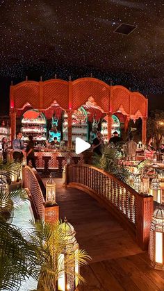 an outdoor dining area at night with lots of lights on the ceiling and palm trees in the foreground