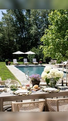 an outdoor dining table set with plates and glasses next to a swimming pool surrounded by trees