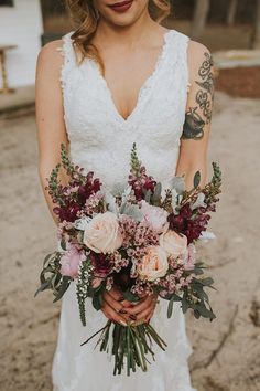 a woman holding a bouquet of flowers in her hands and looking at the camera while wearing a wedding dress