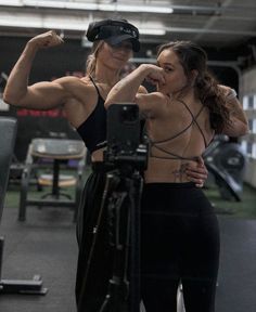 two women flexing their muscles in a crossfit gym with a camera on the side