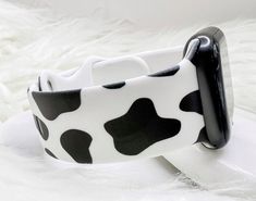 a black and white cow print apple watch band sitting on top of a white fur covered surface